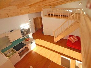 A loft-style room with a kitchen, a red sofa, and a wooden staircase.