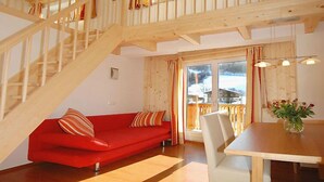 Ein Holzinnenraum mit einem roten Sofa, einem Esstisch und einer Treppe.