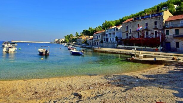 Un pueblo costero con edificios de piedra, mar azul cristalino y barcos anclados cerca de la orilla.