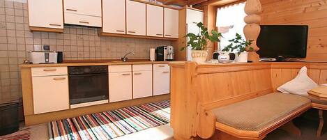 Una cocina compacta con armarios blancos, horno integrado y un comedor con banco.