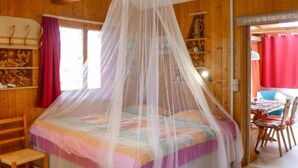 Una habitación con una cama bajo una mosquitera, paredes de madera, una silla y una mesa con sillas.