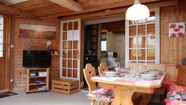 Interior de una cabaña de madera con una mesa de comedor preparada para cuatro personas, un televisor y un cuadro en la pared.