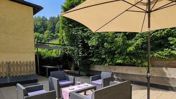 An outdoor patio with wicker furniture, a table, and a large umbrella. - Dr.Steiner by Interhome (Zell am See)