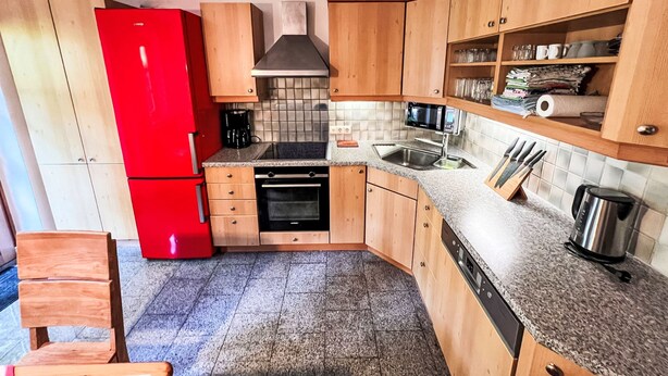Une cuisine compacte avec des meubles de rangement en bois, un réfrigérateur rouge, un four à micro-ondes et un lave-vaisselle.