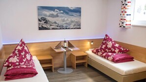 A cozy room with two beds, a small table, and a painting of mountains. - Bella Monte by Interhome (Pettneu am Arlberg)