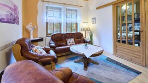 A cozy living room with leather sofas, a round coffee table, and a wooden cabinet with glass doors.