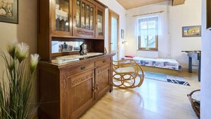 A room with a wooden cabinet, a wicker chair, a bed, and a window with a view.
