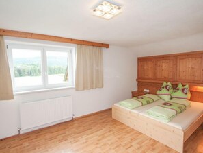 Un dormitorio con una cama de madera, una ventana con cortinas, un radiador y un techo de madera.