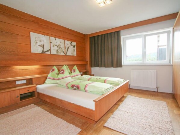 A bedroom with a wooden bed, a nightstand, a window with curtains, and wall art.