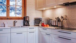 A modern kitchen with white cabinets, a built-in microwave, a coffee maker, and a window with a view of snow-covered trees. - Magicien by Interhome (Nendaz)