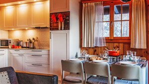 A cozy cabin-style kitchen with wooden cabinets, a dining table set for four, and a window with curtains. - Magicien by Interhome (Nendaz)