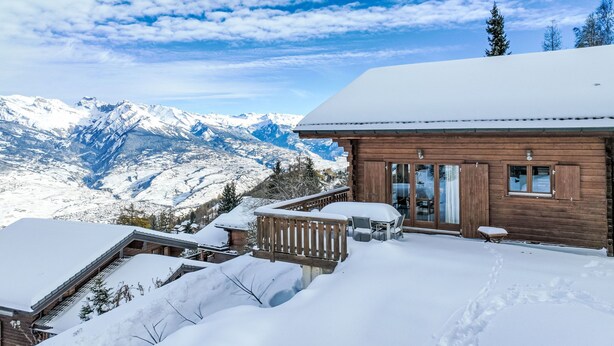 Een houten chalet met een balkon met uitzicht op een besneeerd berglandschap.