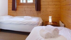 Twee eenpersoonsbedden in een houten kamer met raam en nachtkastje met lamp.