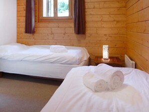 Deux lits simples dans une chambre de chalet en bois, avec une fenêtre et une table de chevet dotée d’une lampe.