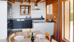 Een moderne keuken met een centraal eiland, een houten eettafel gedekt voor vier personen en een groot raam met gordijnen.