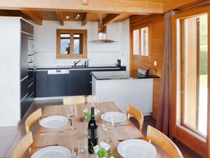 Une cuisine moderne dotée d’un îlot central, d’une table à manger en bois pour quatre personnes et d’une grande fenêtre agrémentée de rideaux.