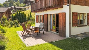 Eine Holzchalet mit Balkon, einer Terrasse mit Gartenmöbeln und Blick auf umliegende Häuser und Bäume.