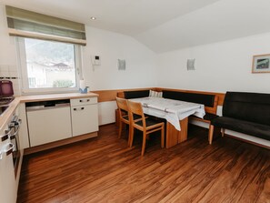A compact kitchen with a dining area, wooden flooring, and a window with a view of houses.
