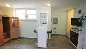 A compact kitchen with a built-in microwave, a small refrigerator, and a sink. There is a wooden cabinet with a mirror and a small table with a chair. A television is mounted on the wall. - Apartment Rosi by Interhome (Werfenweng)