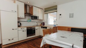 A compact kitchen with white cabinets, a microwave, an oven, and a dining area with a table and chairs. - Apartment Rosi by Interhome (Werfenweng)