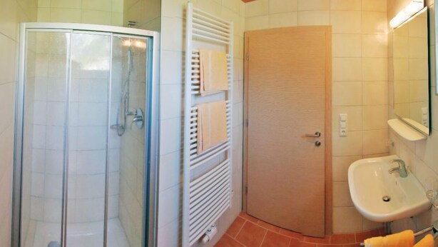 Un baño con cabina de ducha de vidrio, un perchero, una puerta de madera y un lavamanos con espejo.