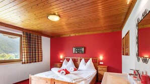 Ein hölzernes Bett, eine rote Wand, ein Fenster mit Karottenvorhängen und ein weißes Waschbecken mit roten Seifenspendern.