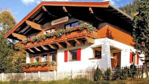 Ein traditionelles Gebäude im alpinen Stil mit einem hölzernen Balkon, roten Fensterläden und einem Schild mit der Aufschrift "Sonnenhang".