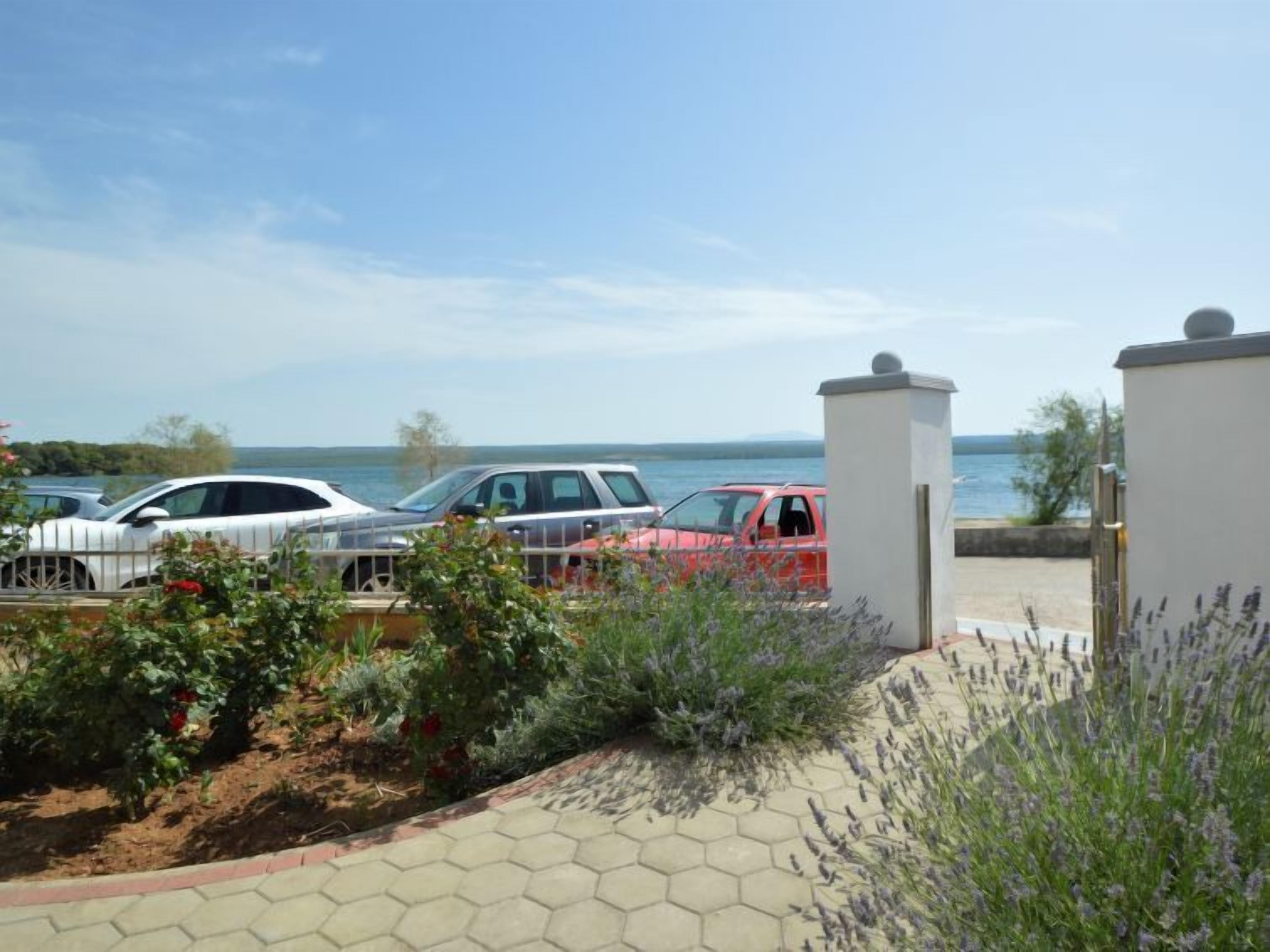 A parking area with cars, a view of the sea, and a garden with lavender.