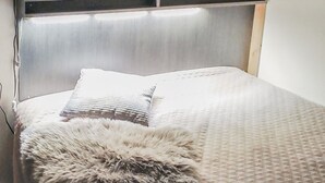 Un lit avec une couverture à motifs et un oreiller moelleux, une tête de lit en bois et une petite étagère au-dessus du lit.