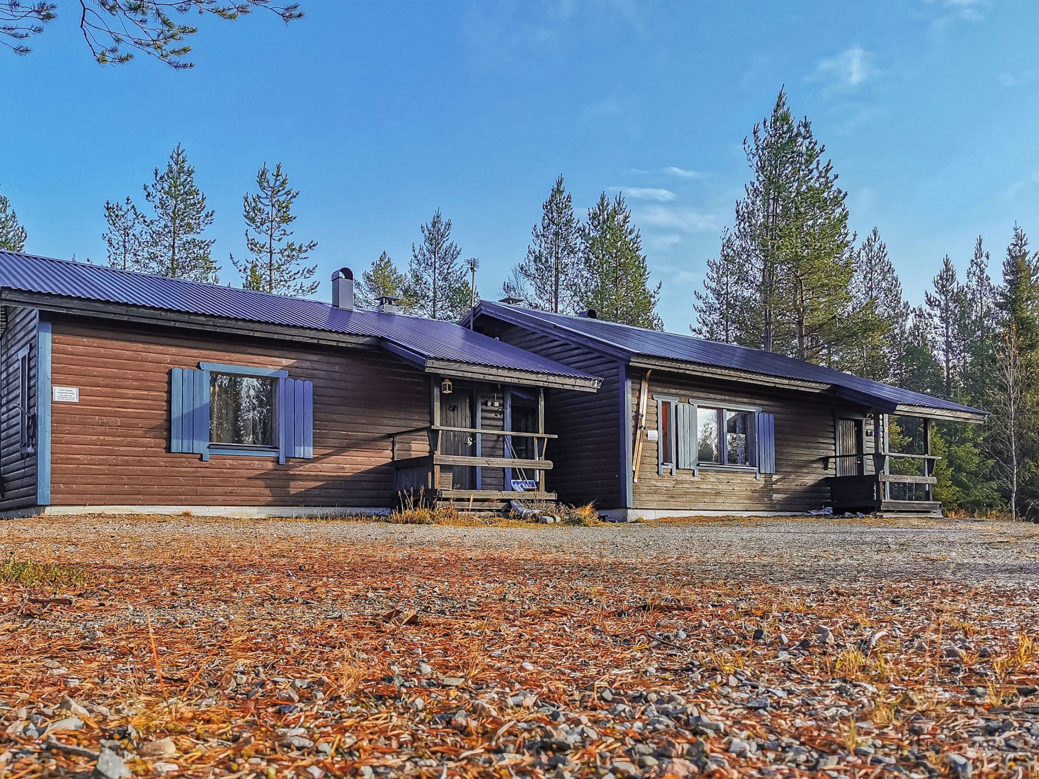 A row of log cabin-style buildings with metal roofs, surrounded by a gravel driveway and pine trees.