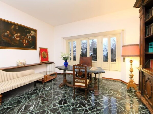 A room with a marble floor, a dining table with chairs, a sofa, a bookshelf, and a painting on the wall.