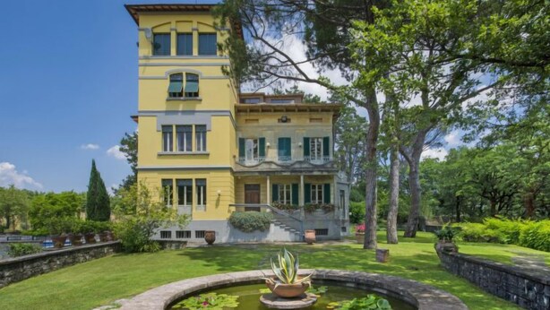 Un bâtiment jaune à deux étages, avec une fontaine en pierre dans le jardin.