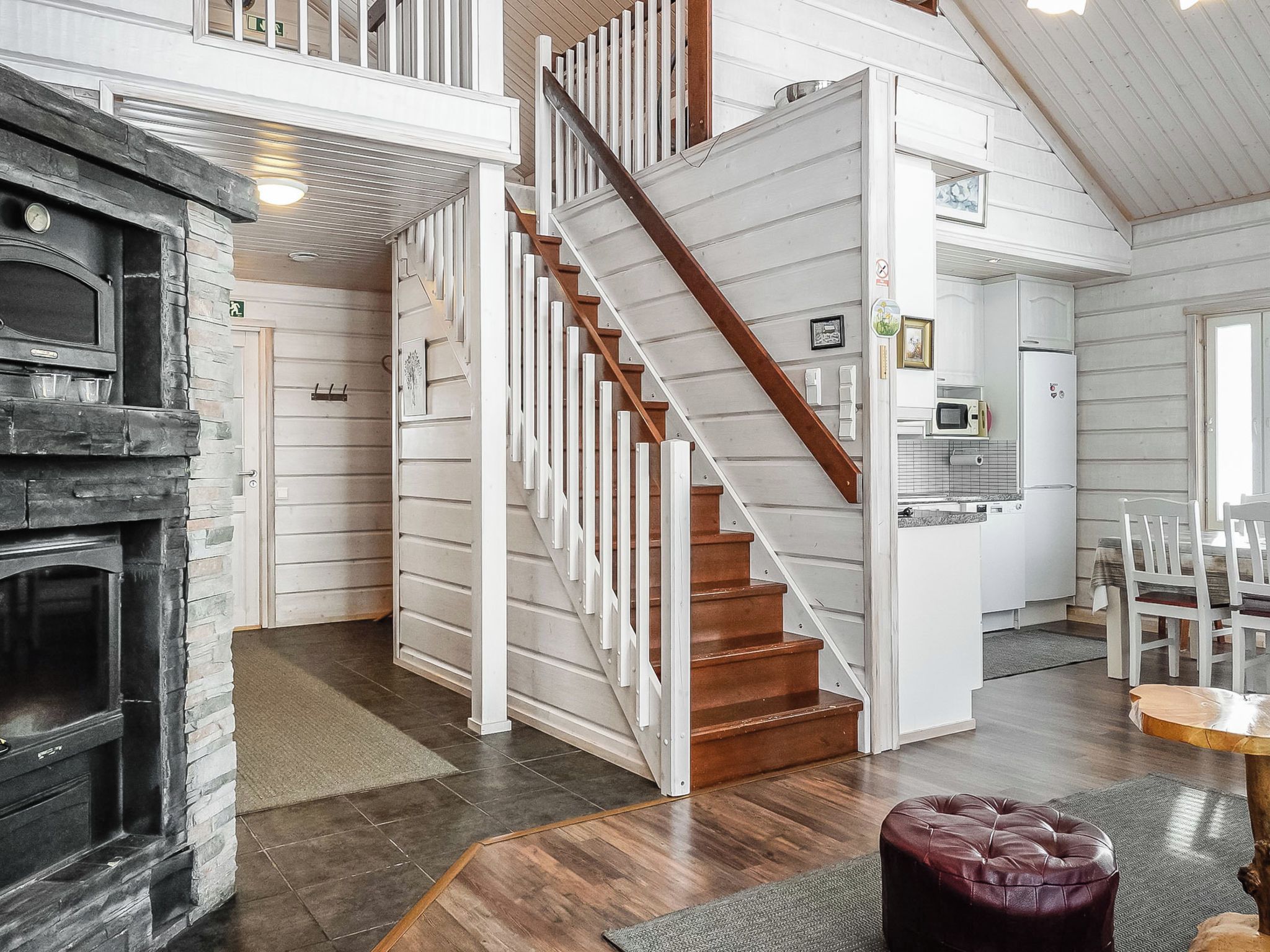 A spacious living area with a wooden staircase, a fireplace, and a kitchen area.