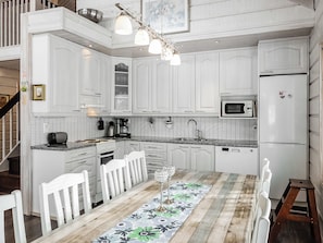 A kitchen with white cabinets, a microwave, a Bosch refrigerator, a dining table with chairs, and a chandelier. - Kerkänperä by Interhome (Sodankylä)