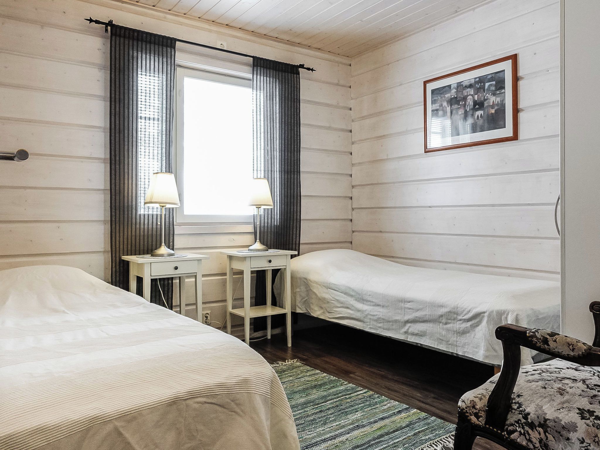 A room with two beds, a desk with two lamps, a framed picture on the wall, and a patterned rug.