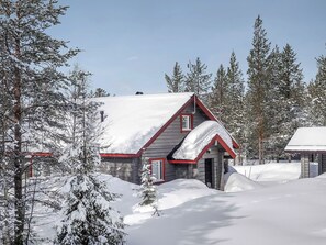 A log cabin with a snow-covered roof, surrounded by snow-laden trees.