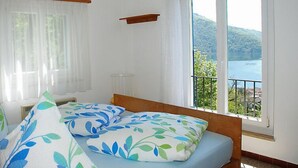 Un dormitorio con cama, ventana con vistas a un lago y colinas, y un pequeño balcón.
