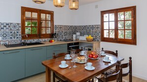 A kitchen with a wooden table set for dining, a coffee machine, and a window with a view of greenery. - Hermine by Interhome (L'Escala)