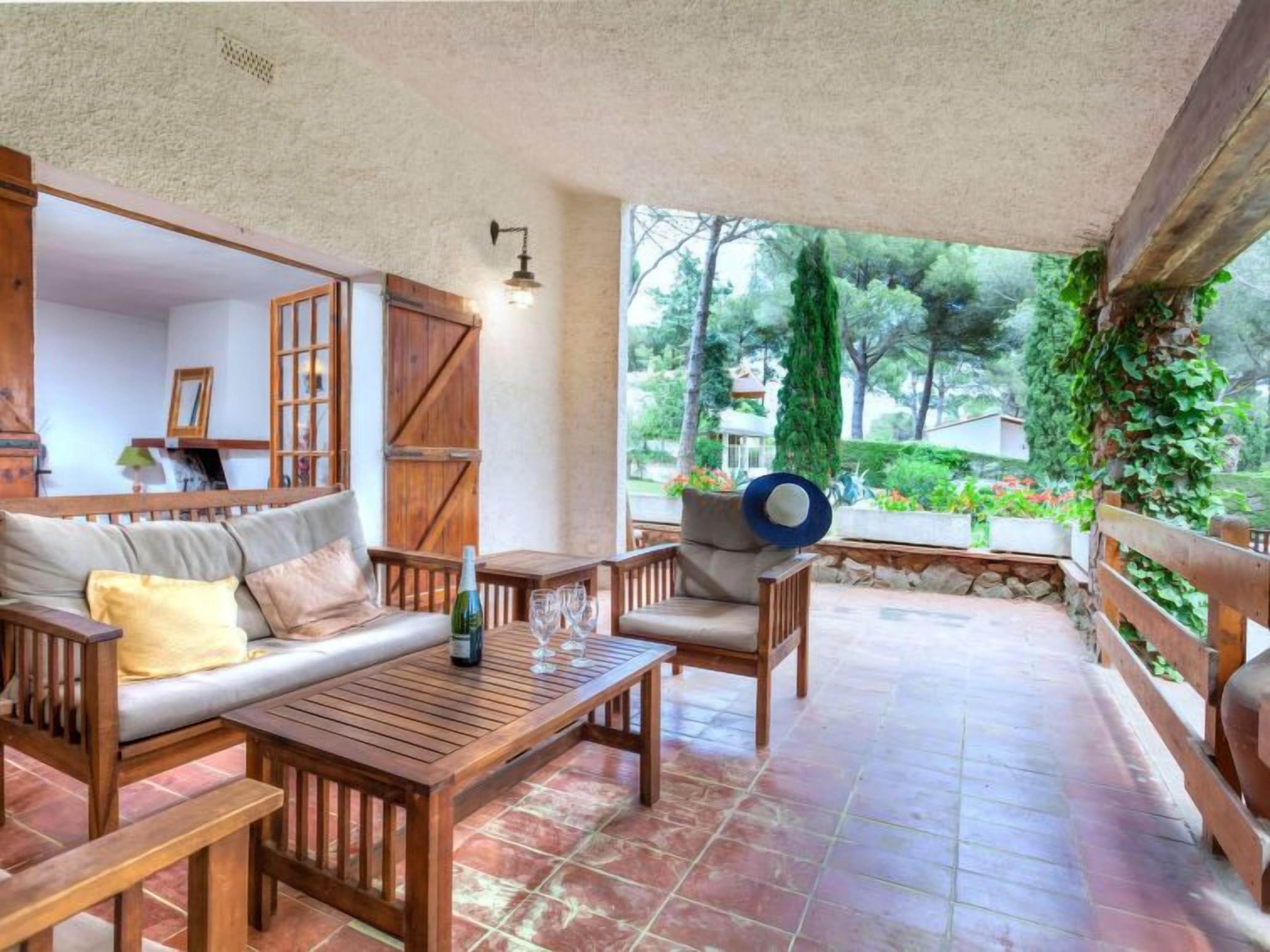A cozy patio with wooden furniture, a table, and a bottle of wine.