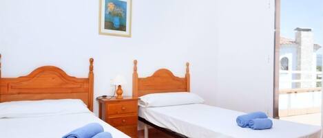 A hotel room with two wooden beds, white linens, a small bedside table with a lamp, and a painting on the wall.