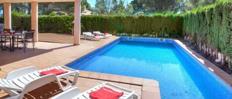 Una piscina con sillones de descanso y una zona de estar techada.