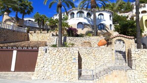 A stone wall with a gate, palm trees, and a white building with arched windows. - Roberto by Interhome (Benissa)