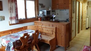 A cozy kitchen with wooden cabinets, a dining table with chairs, and a window with curtains. - Namasté by Interhome (Le Grand Bornand)