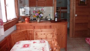 A wooden kitchen with a dining table, a coffee machine, and a vase with flowers. - Namasté by Interhome (Le Grand Bornand)