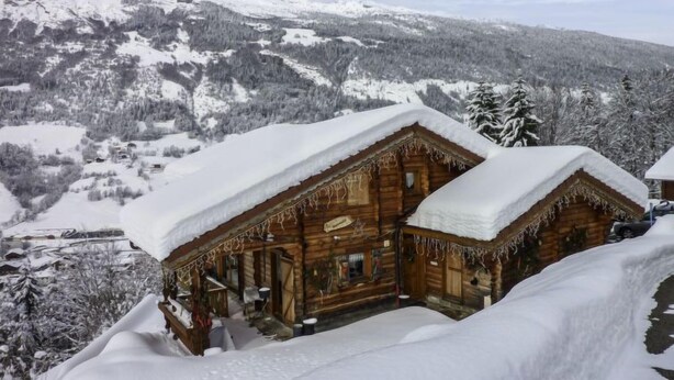 A wooden cabin with a snow-covered roof, surrounded by a snowy landscape and mountains. - Namasté by Interhome (Le Grand Bornand)