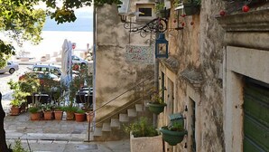 A narrow street with a building featuring a staircase, potted plants, and a sign reading "Hotel Ateliur". - Apartment Sani by Interhome (Karlobag)