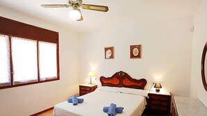 A bedroom with a bed, two bedside tables with lamps, a ceiling fan, and two framed pictures on the wall. - El Rinconcito by Interhome (L'Ampolla)