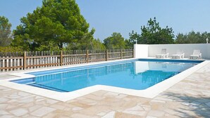A rectangular swimming pool with a white border, surrounded by a stone patio. There are white lounge chairs and a wooden fence in the background. - El Rinconcito by Interhome (L'Ampolla)