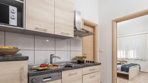 A modern kitchen with a dishwasher, a sink, and a stove. There is a wooden cutting board with vegetables and a bowl of fruit on the counter. - Apartment Tea by Interhome (Krk/Šilo)