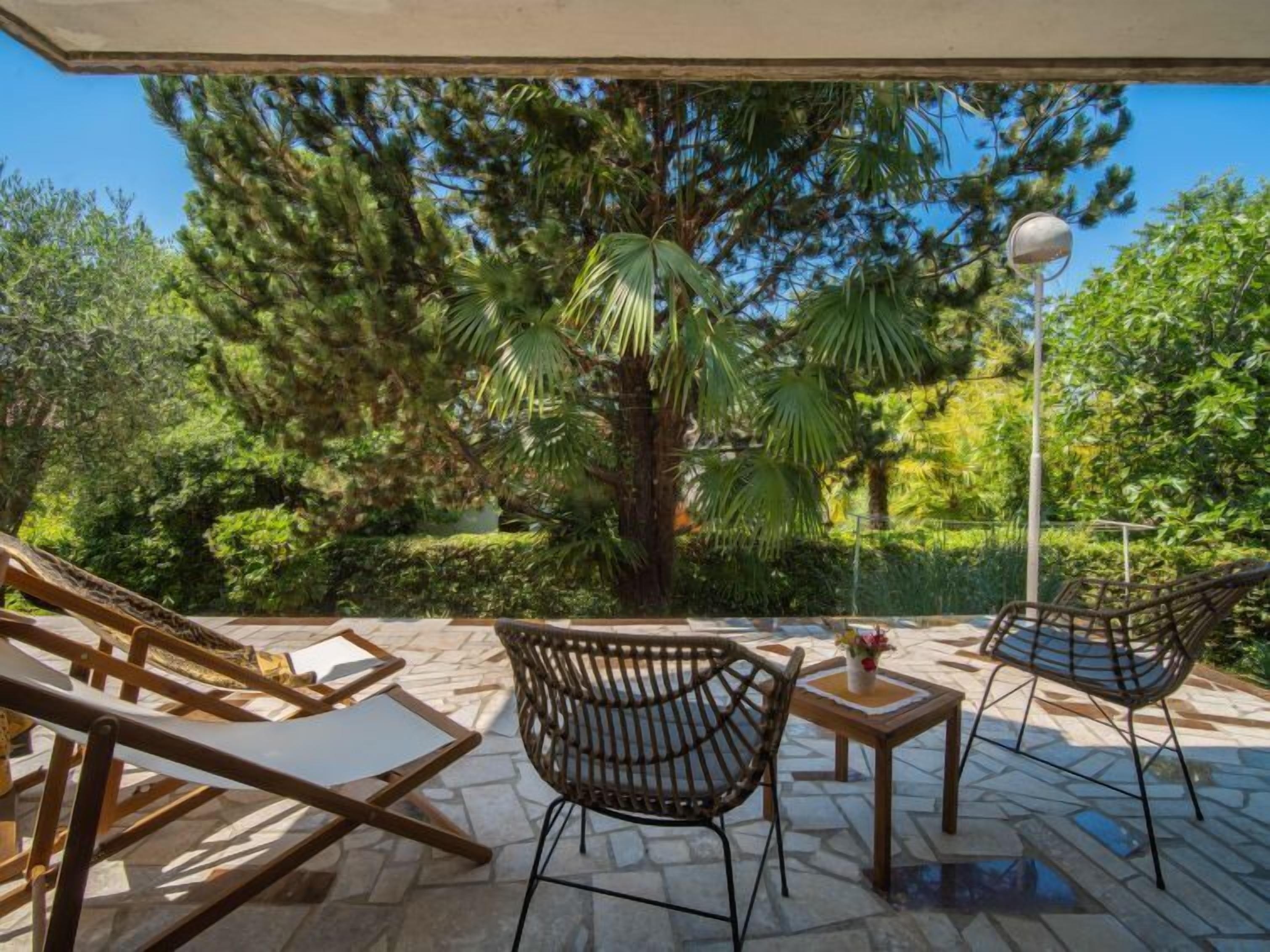Un espace patio aménagé avec des chaises et une table en osier, entouré d’une végétation luxuriante et surplombé d’un ciel bleu azur.